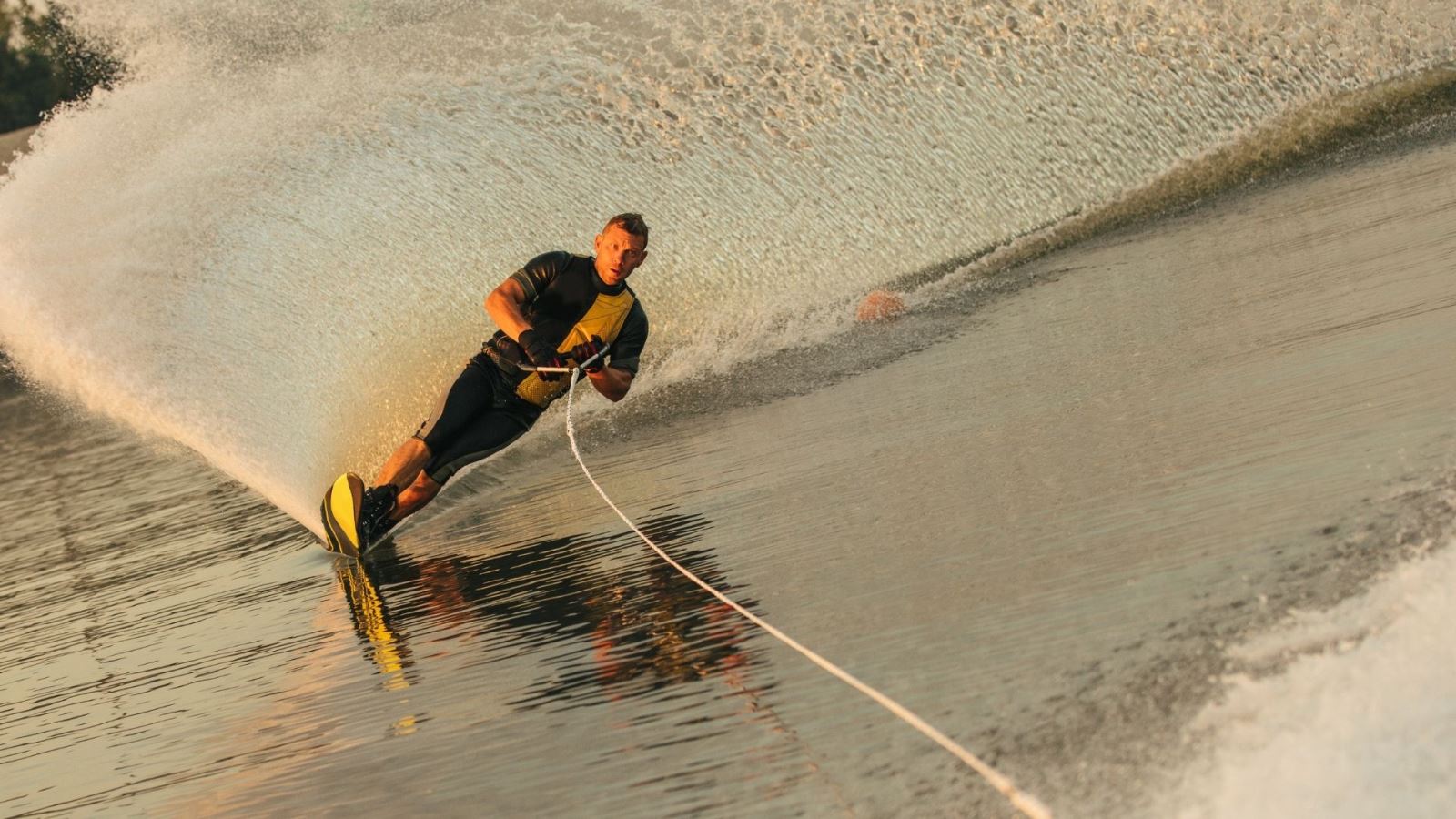 A water skier in a black wetsuit at sunset on golden water
